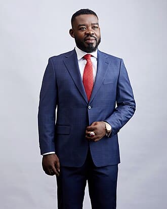 Richard Nii Armah Quaye, standing in a navy suit and red tie against a plain studio background